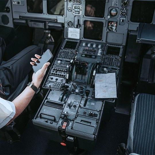 Close-up of the cockpit and the left arm of a pilot reviewing airline document management software on a smartphone